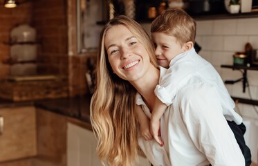 Happy mother and son smiling at each other affectionately. Young mother playing and hugging her cute son in the kitchen at home. Caring single mother bonding with her young son