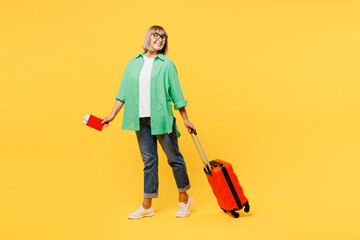 Traveler elderly woman wear green casual clothes hold passport ticket bag isolated on plain yellow background. Tourist travel abroad in free spare time rest getaway. Air flight trip journey concept.