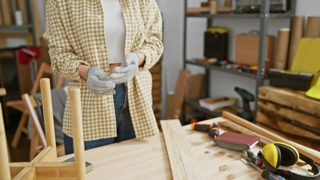 A woman in safety glasses prepares to work in a carpentry workshop surrounded by tools and wood.