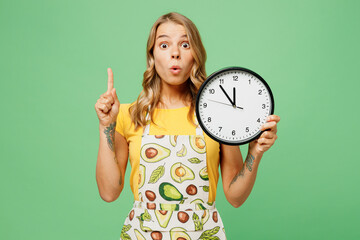 Young housewife housekeeper chef cook baker woman wear apron yellow t-shirt hold in hand clock show...