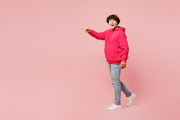 Fototapeta na wymiar Full body surprised side view young Caucasian man wears hoody casual clothes point index finger aside on area mock up isolated on plain pastel light pink background studio portrait. Lifestyle concept.