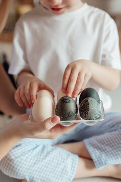 Preparing for Easter. Family at home. Easter Family traditions. Closeup photo of mother and son holding hands painted multi-colored Easter eggs smiling in cozy light kitchen at home.