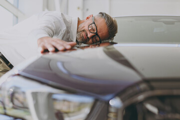 Close up adult happy man customer male buyer client wear shirt glasses put head on car hood choose...