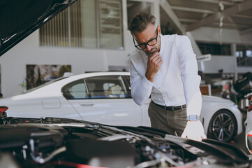 Adult thoughtful man customer male buyer client wear shirt examining engine open car hood choose auto want to buy new automobile in showroom vehicle salon dealership store motor show. Sales concept.