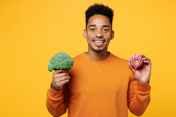 Young fun happy man wear orange sweatshirt casual clothes hold in hand broccoli donut isolated on plain yellow background studio portrait. Proper nutrition healthy fast food unhealthy choice concept.