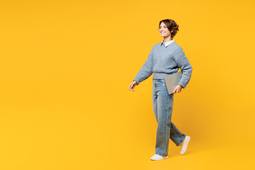 Fototapeta na wymiar Full body side view young IT woman she wears grey knitted sweater shirt casual clothes hold use work on laptop pc computer walk isolated on plain yellow background studio portrait. Lifestyle concept.