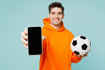 Young man fan wears hoody casual clothes use blank screen mobile cell phone cheer up support football sport team hold in hand soccer ball watch tv live stream isolated on plain blue color background.