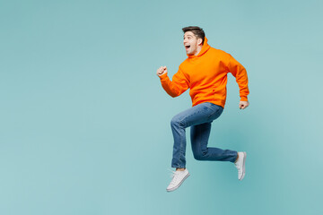 Fototapeta na wymiar Full body side profile view excited fun young man he wears orange hoody casual clothes jump high run fast isolated on plain pastel light blue cyan color background studio portrait. Lifestyle concept.