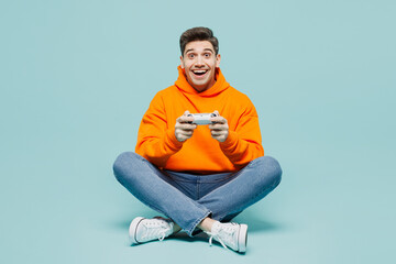 Full body excited young man wear orange hoody casual clothes sitting use play racing app on mobile...