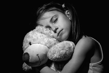 The pain of loneliness. A crying chld girl hugs a Teddy bear toy. Black and white horizontal image.