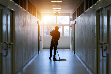 Janitor man mopping floor in hallway office building or walkway after school and classroom silhouette work job with sun light background. Poor people working job.