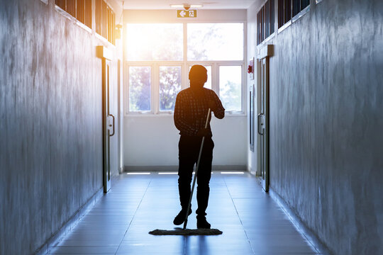 Janitor man mopping floor in hallway office building or walkway after school and classroom silhouette work job with sun light background. Poor people working job.