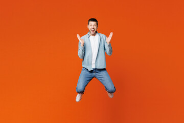 Fototapeta na wymiar Full body excited overjoyed young man he wearing blue shirt white t-shirt casual clothes jump high look camera spread hands isolated on plain red orange background studio portrait. Lifestyle concept.