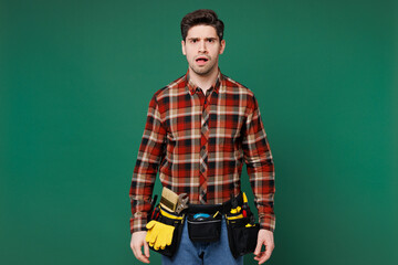 Young sad mad furious indignant employee laborer handyman man wear red shirt look camera isolated on plain green background. Instruments accessories for renovation apartment room. Repair home concept. - obrazy, fototapety, plakaty
