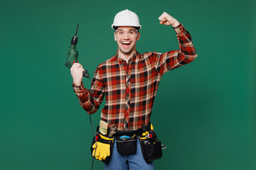 Young employee laborer handyman man wearing red shirt hardhat hat use hold electric drill isolated...