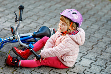 Cute little girl sitting on the ground after falling off her bike. Upset crying preschool child...