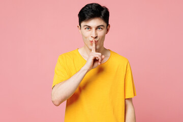 Young Caucasian man wears yellow t-shirt casual clothes say hush be quiet with finger on lips shhh...