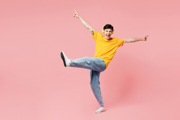 Full body young fun man he wears yellow t-shirt casual clothes listen to music in headphones with outstretched hands isolated on plain pastel light pink background studio portrait. Lifestyle concept.
