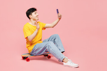 Full body young man he wear yellow t-shirt casual clothes sit on skateboard doing selfie shot on...