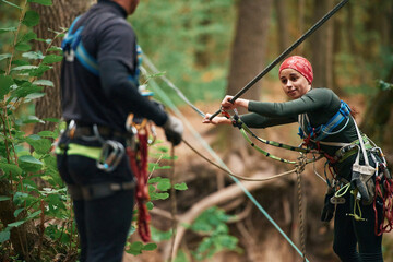 Preparing the ropes. Man and woman doing climbing in forest with use of safety equipment