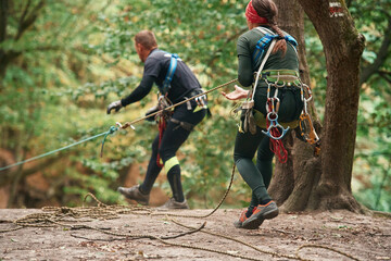 Setting up the ropes. Man and woman doing climbing in forest with use of safety equipment