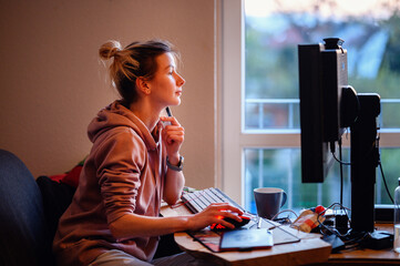 Young woman with funny ponytail sits before computer and do online shopping in homeward