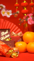 Chinese Lunar New Year background. ancient Chinese gold bar in silk bag, red gift box with text best wishes, orange, paper fan, plum blossom branch, candle and ornament hanging at background