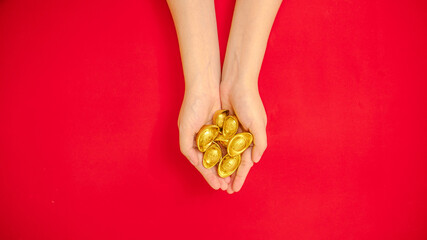 flat lay of hand holding a lot of ancient Chinese ingot gold bar out from the top side for Chinese Lunar New Year celebration background, red theme with copy space