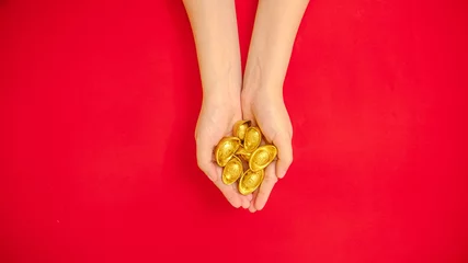 Foto op Canvas flat lay of hand holding a lot of ancient Chinese ingot gold bar out from the top side for Chinese Lunar New Year celebration background, red theme with copy space © asiandelight