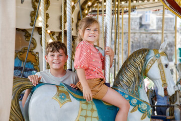Happy positive preschool girl having a ride on the old vintage merry-go-round in city of St Malo France. Smiling child on a horse. - obrazy, fototapety, plakaty