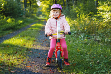 Child riding balance bike. Kids on bicycle in sunny forest. Little girl enjoying to ride glider...