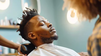 Fototapeten African American man sitting in chair and getting haircut in salon © Sasint