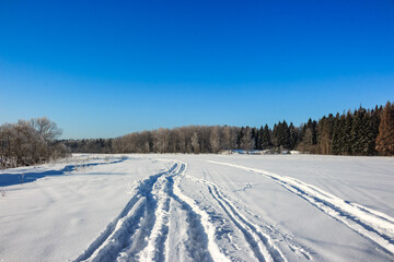 Winter landscape with a view of a snow-covered field against the backdrop of a forest with footprints in the snow