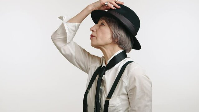 Mature lady in a crisp white shirt and hat, holding hat brim, isolated on a white background. High quality 4k footage