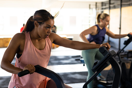 Determined biracial young woman exercising on elliptical trainer machine in gym, copy space