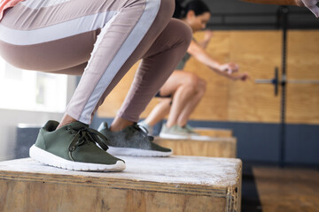 Low section of biracial young woman practicing squats on wooden plyo boxes in gym, copy space