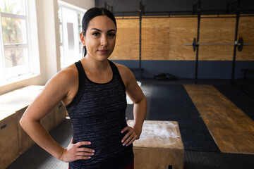 Portrait of confident caucasian young woman with hands on hip standing by plyo box in gym