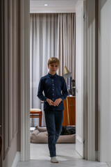 In the comforting ambiance of a softly lit home, a young boy pauses at the doorway, exuding...
