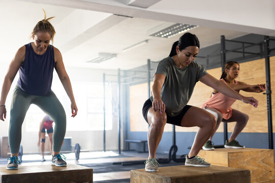 Full length of diverse women practicing squats on wooden plyo boxes in gym, copy space