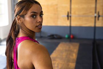 Portrait of biracial young woman confidently looking over shoulder while standing in health club