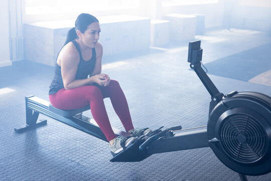 Tired caucasian young woman sitting on rowing machine in health club, copy space