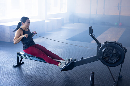 Dedicated caucasian young woman exercising on rowing machine in health club