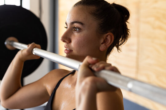 Closeup of dedicated caucasian young woman lifting barbell confidently in health club