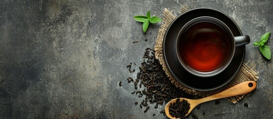 Black tea cup and wooden spoon with tea leaves on rustic table with space for text. - Powered by Adobe