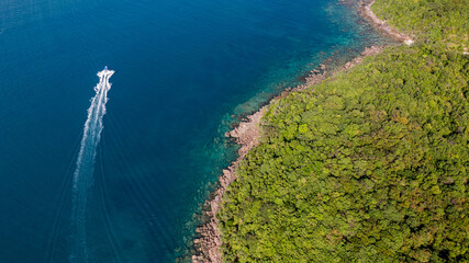 Aerial view of a speedboat creating a white wake near a lush green coastline, showcasing the...