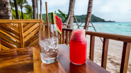 Refreshing summer drinks on a wooden table against a tropical beach backdrop, symbolizing vacation...