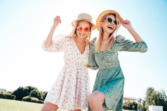 Two young beautiful smiling hipster woman in trendy summer dress. Carefree women in the street in hats. Positive models at sunset. Cheerful and happy. Bottom view. They look at camera from above