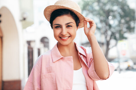 Young beautiful smiling hipster woman in trendy summer pink costume clothes. Carefree female posing in the street at sunny day. Positive model outdoors at sunset. Cheerful and happy in hat