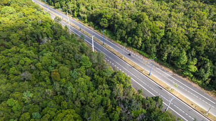 Aerial view of a multi-lane highway cutting through a dense forest with a single motorcycle on the...