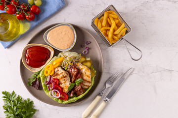 Poultry burger without a bun, served on a plate with bacon, vegetables and fries.